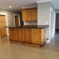 A kitchen island with wood cabinets, black countertop, and a sink, set on a polished concrete floor in a modern room.