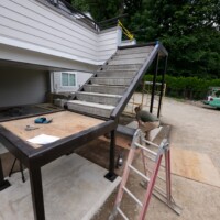 A person works on installing a metal-framed staircase attached to a raised deck outside a house.