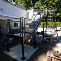 Outdoor metal staircase under construction next to a house, with tools, materials, and a ladder nearby.