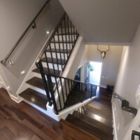 A view looking down a modern wooden staircase with metal railings and a mounted antler decor on the wall.