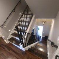 A view looking down a modern wooden staircase with metal railings and a mounted antler decor on the wall.