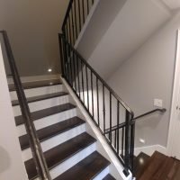 A staircase with dark wooden steps, white risers, and a black metal railing, adjacent to a light gray wall.