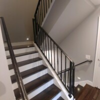 A staircase with dark wooden steps, white risers, and a black metal railing, adjacent to a light gray wall.