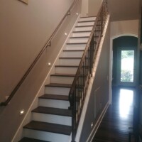 A wooden staircase with metal railings and wall-mounted lights leads to an upper floor in a modern home.