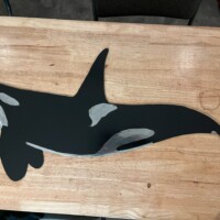 A flat, black and white painted cutout of an orca whale lies on a wooden table.